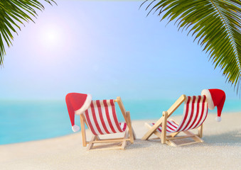 Two striped red-white sunloungers with Christmas Santa hats for romantic couple at ocean sandy sunset beach under big palm leaves, New Year travel destinations concept for vacation in hot countries