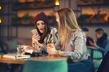 Two friends enjoying coffee together in a coffee shop and using