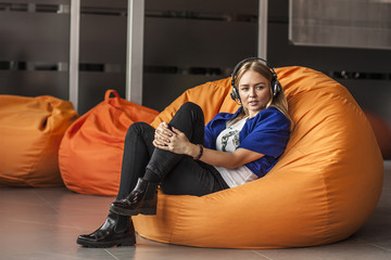 Armchair traditional bean bag for fun and relaxation  orange color. Young woman  with headphones while sitting on big cushioned frameless chair
