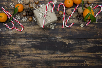 Christmas gift, tangerines, nuts and candy canes on brown wooden background