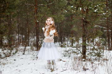 Attractive young girl in wintertime outdoor. A girl in the winter forest smiling and cheering.  Snow is falling