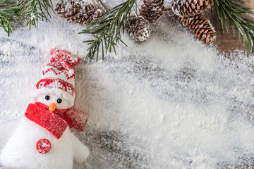 red and white snowman and a snowy fir branch with pine cones on a snow background