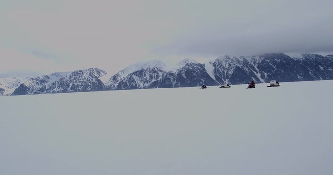 Group of snow machines racing over sea ice near mountains