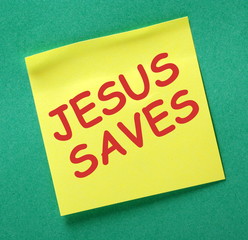 The words Jesus Saves in red text on a yellow sticky note posted on a green noticeboard