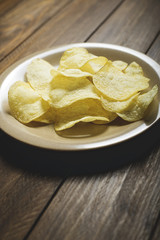 A plate with chips standing on dark brown wooden table. Vertical studio shot