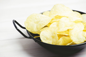 Close-up of a small pan with chips standing on pale gray wooden table. Horizontal studio shot