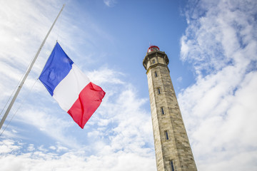 view from the ground of the 1854 Grand Phare des Baleines lighthouse with a French flag floating in...