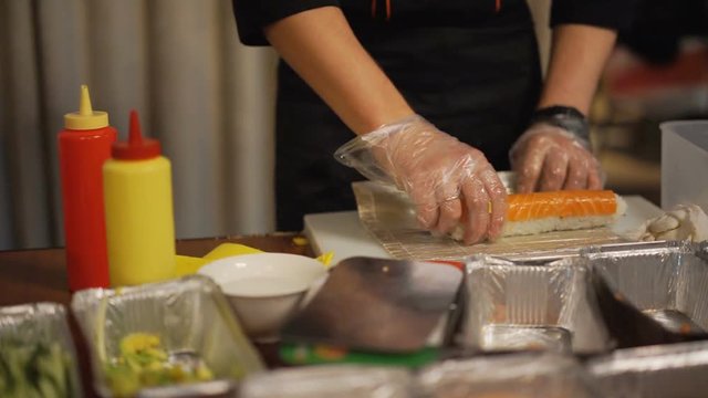 Street sushi vendor forming rolls with bamboo mat, professional cook, fast food