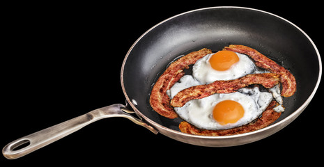Pair of Sunny Side Up Eggs Fried with Four Bacon Rashers in Old Heavy Duty Steel Frying Pan Isolated on Black Background
