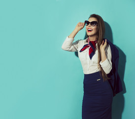 Happy stewardess with sunglasses on blue background looking left.