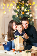 Family of mother, father and little child near Christmas tree with presents, decorations and New Year or Christmas