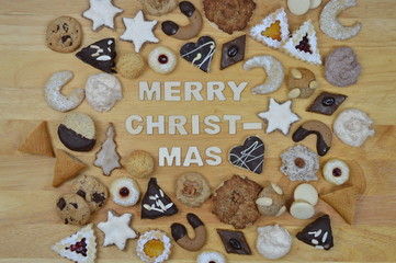 different kinds of Christmas cookies on a breadboard around the words: MERRY CHRISTMAS