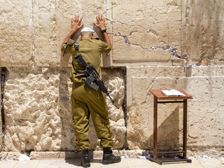 Soldier alone with M16 rifle is praying at the Wailing Wall with his hands on the wall, Jerusalem....