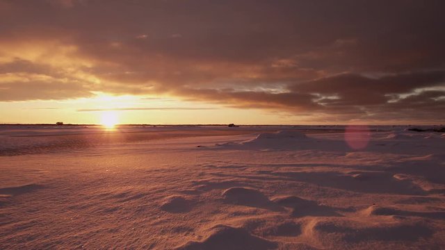 Slow wide pan across snowy tundra landscape at sunset