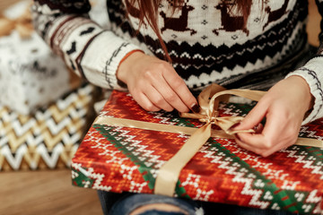 Beautiful girl in reindeer winter sweater unwrapping christmas p