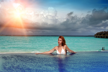 The young beautiful woman in the pool before the sea at sunset