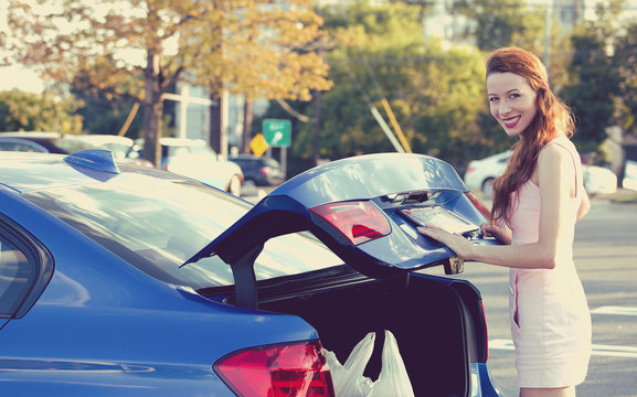 Happy Woman Putting Shopping Bags Inside Car Trunk