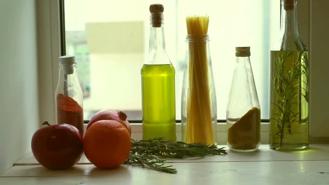 Food ingredients near kitchen window. Cooking oil and kitchen herbs. Extra virgin olive oil in glass bottle. Rosemary herb and garnet fruit. Raw spaghetti. Cooking ingredients
