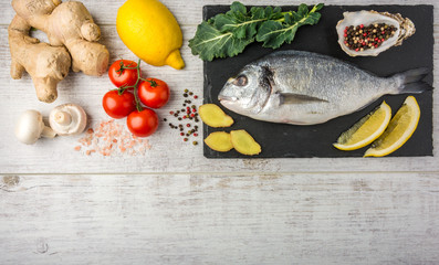 Useful dorado fish, rich in protein, vitamins, Omega 3 with vegetables, lemon and ginger, prepared for cooking on a white wooden table. Top view. Copy space