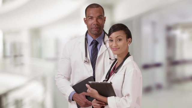 Two African American doctors posing for a portrait while holding their tablets. Black medial experts standing in the hospital with their pads