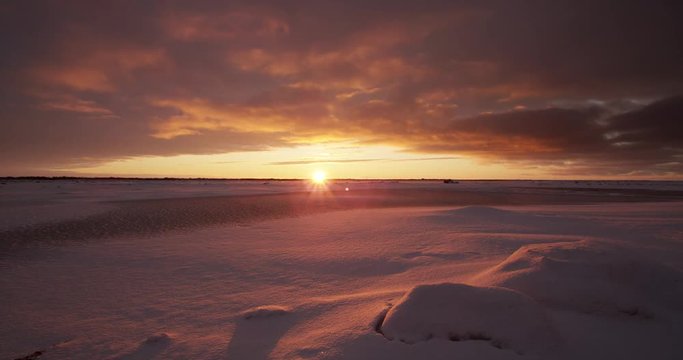 Time lapse of clouds rushing over tundra at sunset with snow
