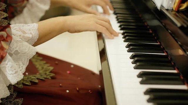 A female pianist, wearing clothes of the 18th century nobility, playing a piano.
