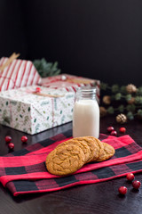 Gingersnap cookies with a glass bottle of milk on a plaid pattern hand towel with decorative cranberries and presents in the background