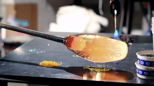 Glassblower rolling molten glass on pieces of colored glass