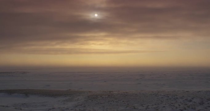 Pan across tundra and sea ice during sunset blizzard