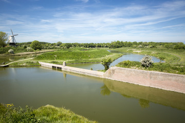 Typical Dutch countryside landscape with a canal, fortified wall and a windmill