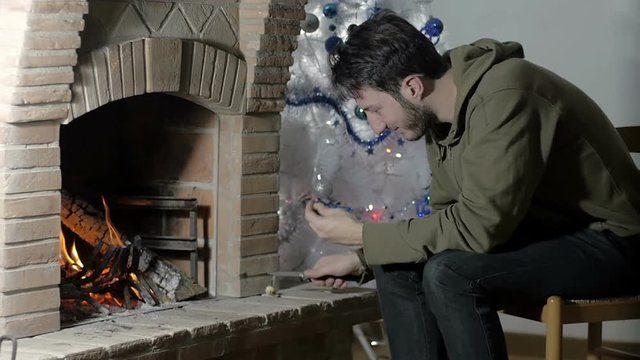 young man sat at home near a fire place, plays pensively with a stick
