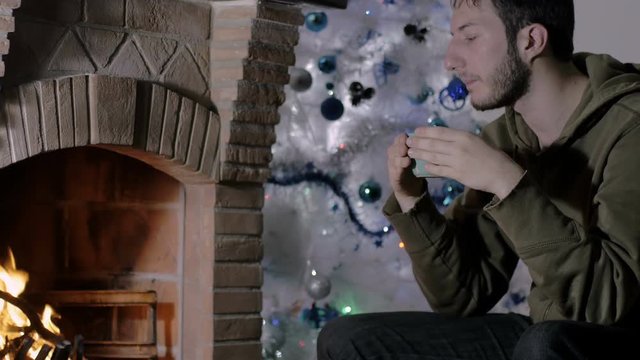 young man in pensive attitude sips a cup of tea, fireplace