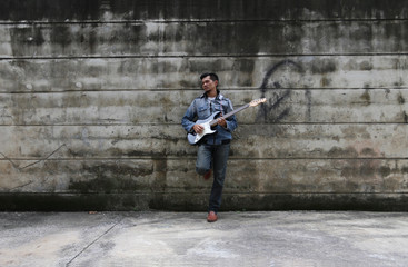 Fototapeta na wymiar A young man wearing jeans, playing a guitar on a brick wall back