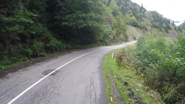 Narrow winding road in mountains surrounded by trees, dangerous driving