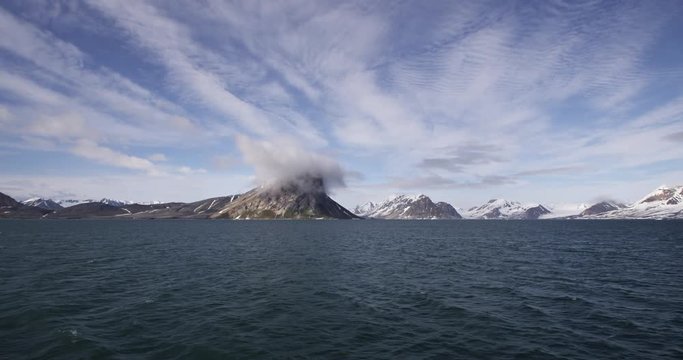 Rocky arctic mountain range across sea with one gray cloud over peak
