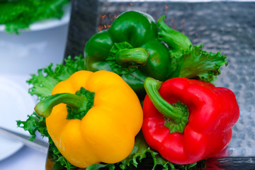 Three colored peppers on table and lettuce