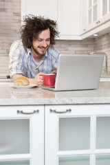 Fototapeta premium Man Eating Breakfast Using Laptop, Man in kitchen drinking coff