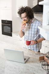 Fototapeta na wymiar Man Eating Breakfast Using Laptop, Man in kitchen drinking coff