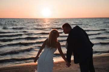 Fototapeta premium young couple stands at the sea beach looking at sunset