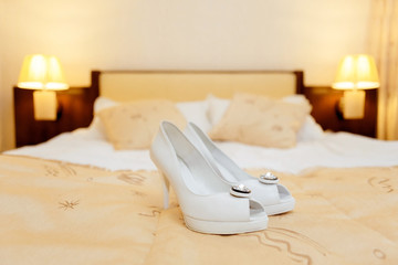 White shoes of the bride standing on the bed in the room