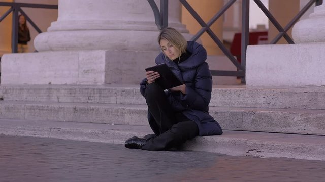 young woman using tablet pc sitting on the stairs of St. Peter square in Rome