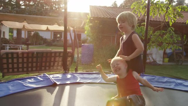 A boy irritates his younger brother, who intentionally falls against him while they are both on a trampoline. 4k. Slow motion.