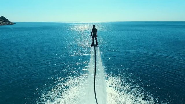 Aerial: Man standing over the water on flyboard.