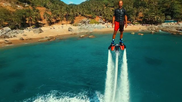Aerial: Man standing over the water on flyboard near the beach.
