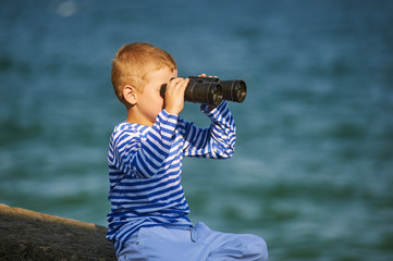 little boy with binoculars , the sea in the background