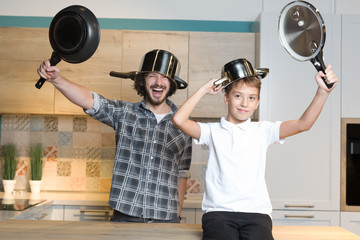 Father and son having fun in kitchen playing with pots