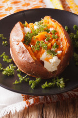 Whole sweet potato baked with cheese, spices and parsley close-up on a plate. vertical