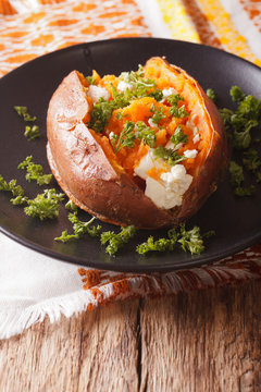 Orange sweet potatoes baked with cream cheese, spices and herb close-up on a black plate. vertical