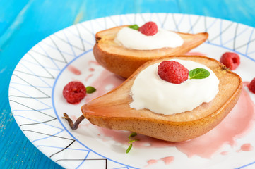 Sweet Baked pear with cream, raspberry syrup, fresh raspberries in sugar and mint leaves. Dessert on a blue wooden background. Close up