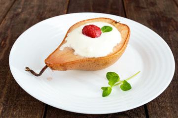 Sweet Baked pear with cream, raspberry syrup, fresh raspberries and mint leaves. Dessert on a dark wooden background.